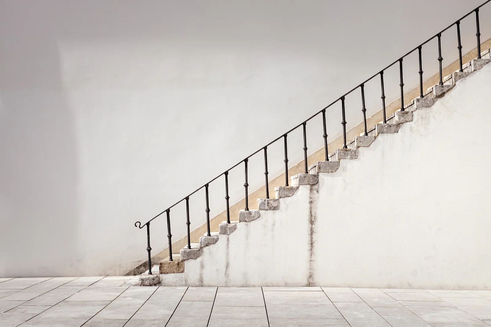 A flight of stone steps with a black iron handrail rises against a plain pale wall.